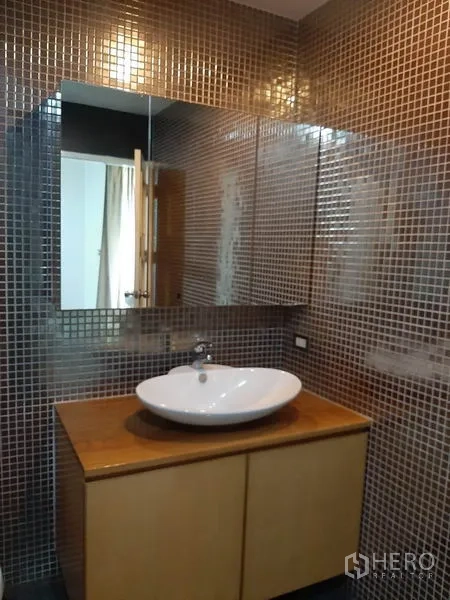 Condominium for rent in Phaya Thai, Bangkok - Bathroom vanity with vessel sink on a wooden cabinet and brown mosaic tile walls.