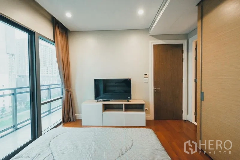 Condominium for rent in Khlong Toei, Bangkok - Master bedroom wall-mounted TV console opposite the bed with door to ensuite.