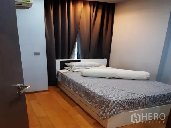 Condominium for rent or sale in Khlong Toei, Bangkok - Cozy bedroom with queen bed, blackout curtains and warm wood flooring.