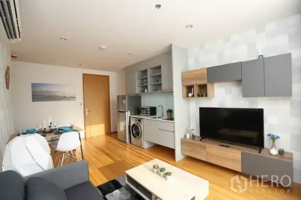 Condominium for rent or sale in Bang Rak, Bangkok - Open living space with TV wall unit, compact kitchen and dining table in bright natural light.