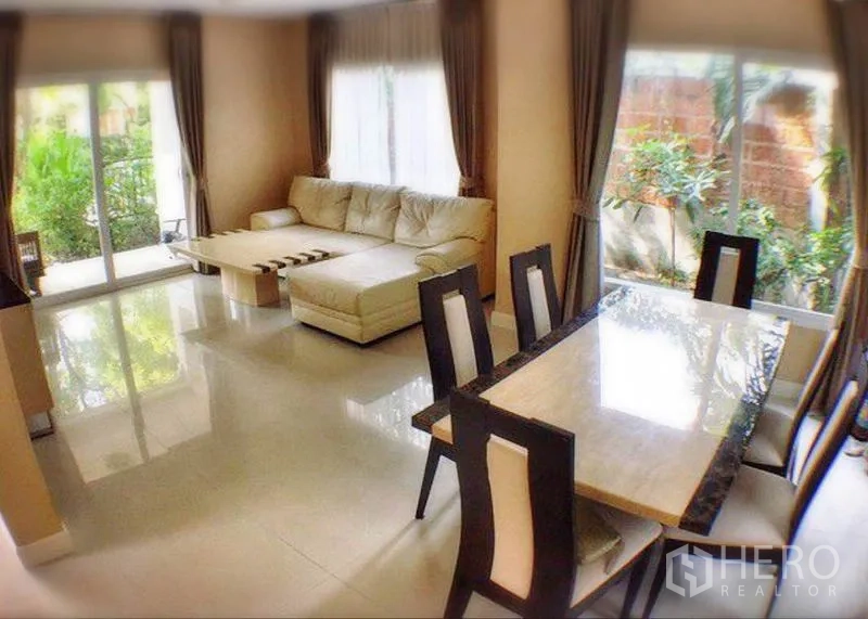 Detached House for rent or sale in Bang Yai, Nonthaburi - Open-plan living and dining area with corner sofa, large windows and garden views.