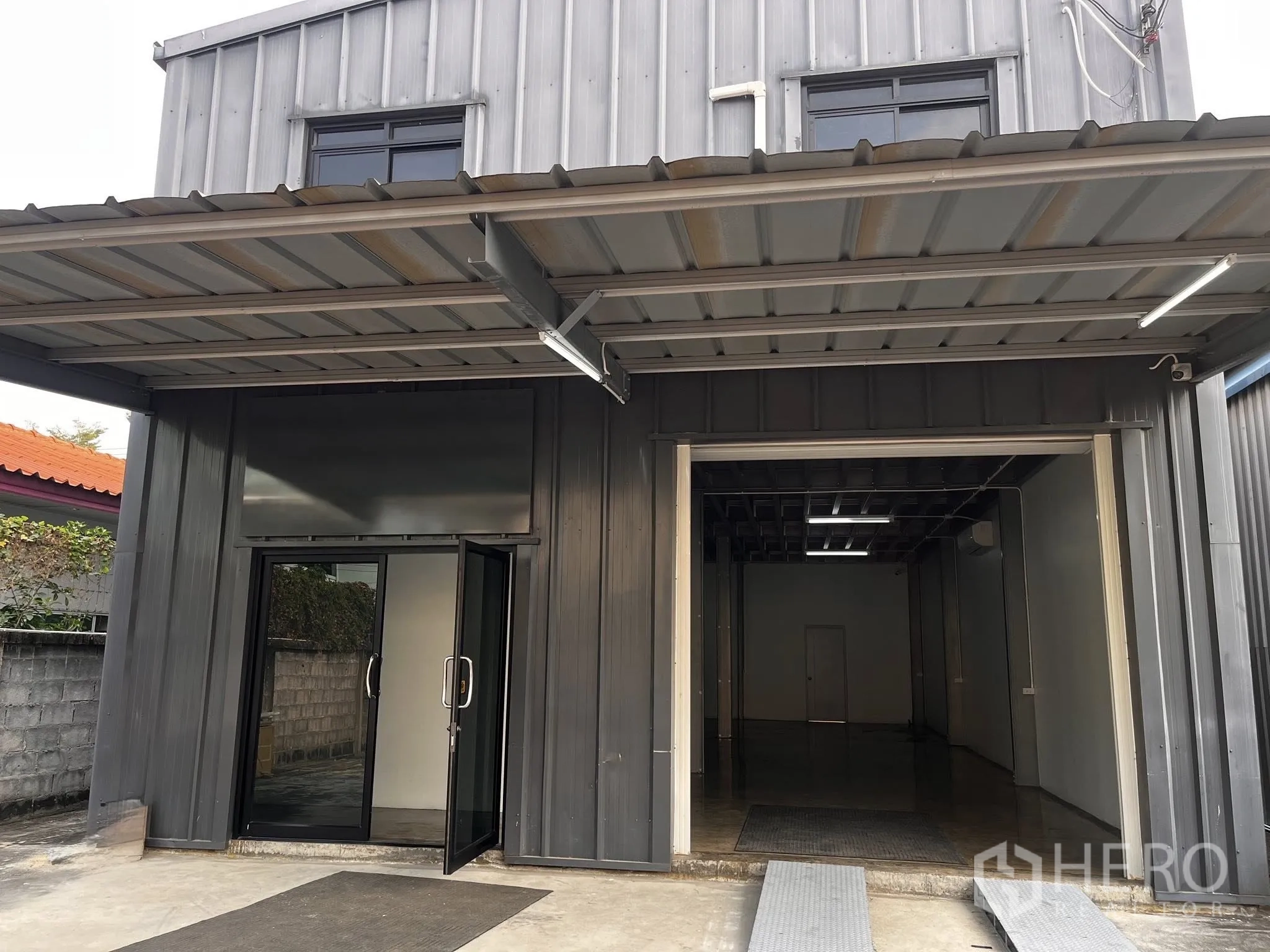 Warehouse for rent in Lat Phrao, Bangkok - Front of the warehouse with a covered canopy, glass entrance door, and roller shutter opening.