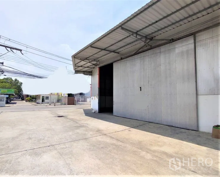 Warehouse for rent in Pathum Thani - Front of a warehouse unit with sliding metal door and canopy, easy truck access from paved drive.