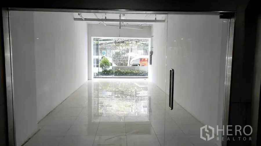 Retail Space for rent in Khlong Toei, Bangkok - Interior view of compact white retail space with polished tiles, track lighting, and front window facing greenery in Khlong Toei, Bangkok.