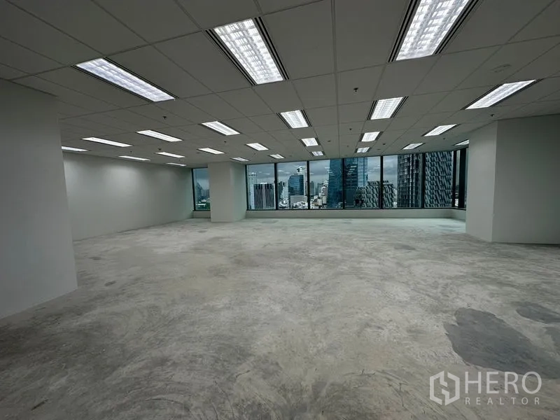 办公空间 出租 - 未装修的办公楼层，荧光灯吊顶，宽幅玻璃窗外是城市景观。