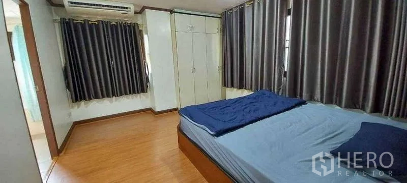 Condominium for rent in Khlong Toei, Bangkok - Master bedroom with wood floors, built‑in wardrobes, large bed, dark curtains and air conditioning.