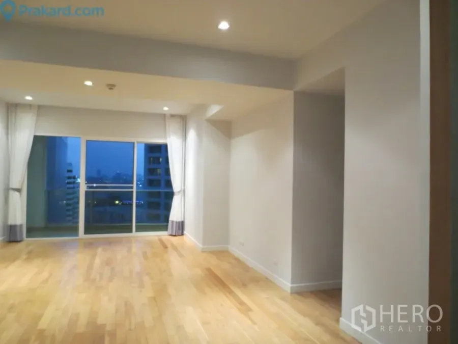 Condominium for rent in Khlong Toei, Bangkok - Spacious living area with light wood floors, recessed lighting and sliding doors to a balcony with evening city views.