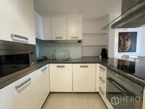 Condominium for rent or sale in Watthana, Bangkok - U-shaped kitchen featuring white cabinetry, stone countertops, oven, cooktop, and sink.