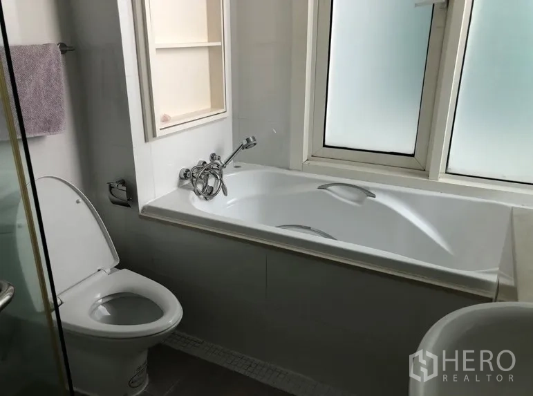 Condominium for rent or sale in Khlong Toei, Bangkok - Modern bathroom with bathtub, toilet and frosted window for natural light.