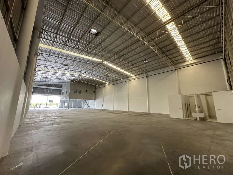 Factory for rent in Khlong Luang, Pathum Thani - Clear-span industrial hall with bright strip lighting, white walls, and a restroom block.