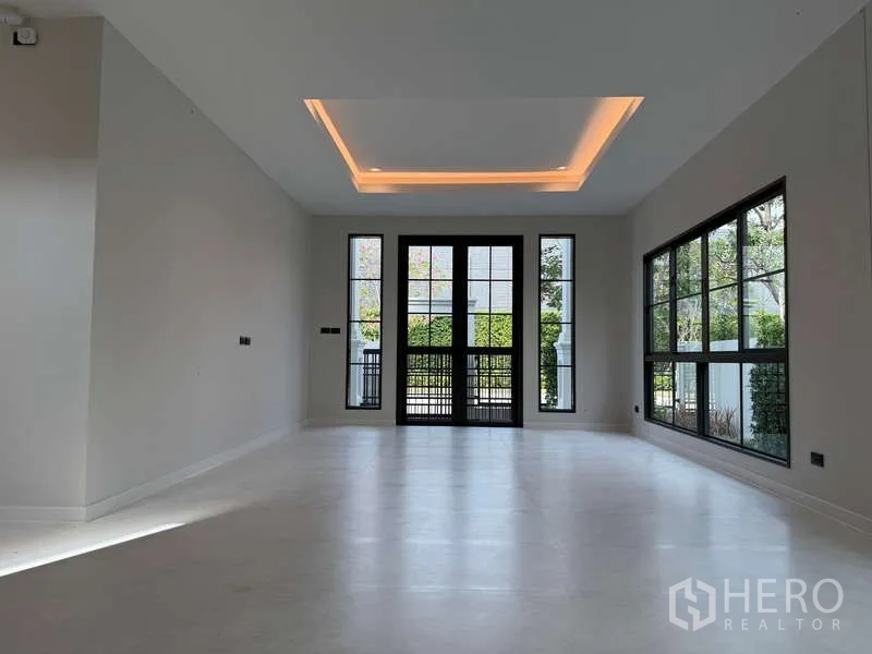独立式住宅 出租或出售在Bang Phli, Samut Prakan - 大客厅，黑色框架落地窗与层级天花灯带。