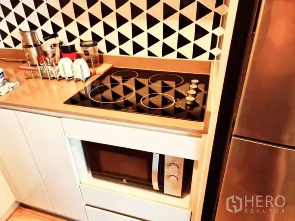 Condominium for sale in Bang Rak, Bangkok - Modern kitchenette featuring electric ceramic cooktop, microwave, geometric backsplash and tall refrigerator.