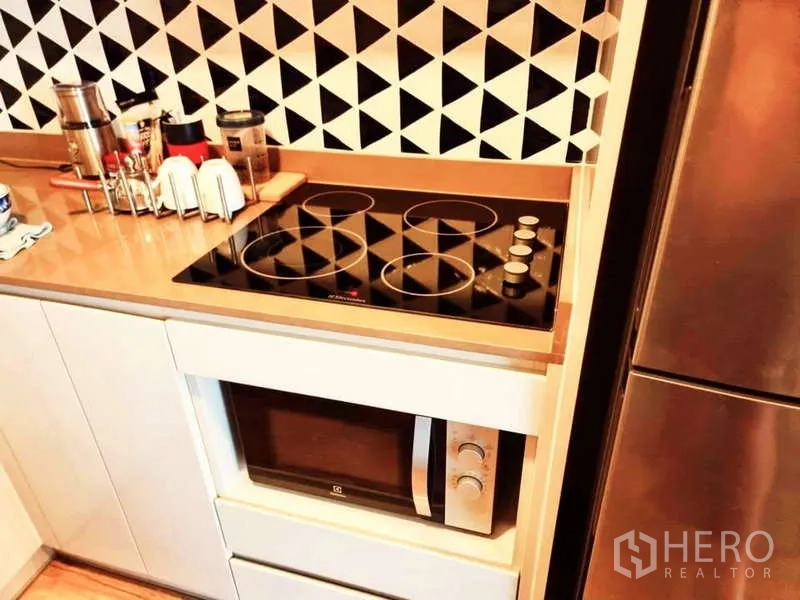 Condominium for sale in Bang Rak, Bangkok - Modern kitchenette featuring electric ceramic cooktop, microwave, geometric backsplash and tall refrigerator.