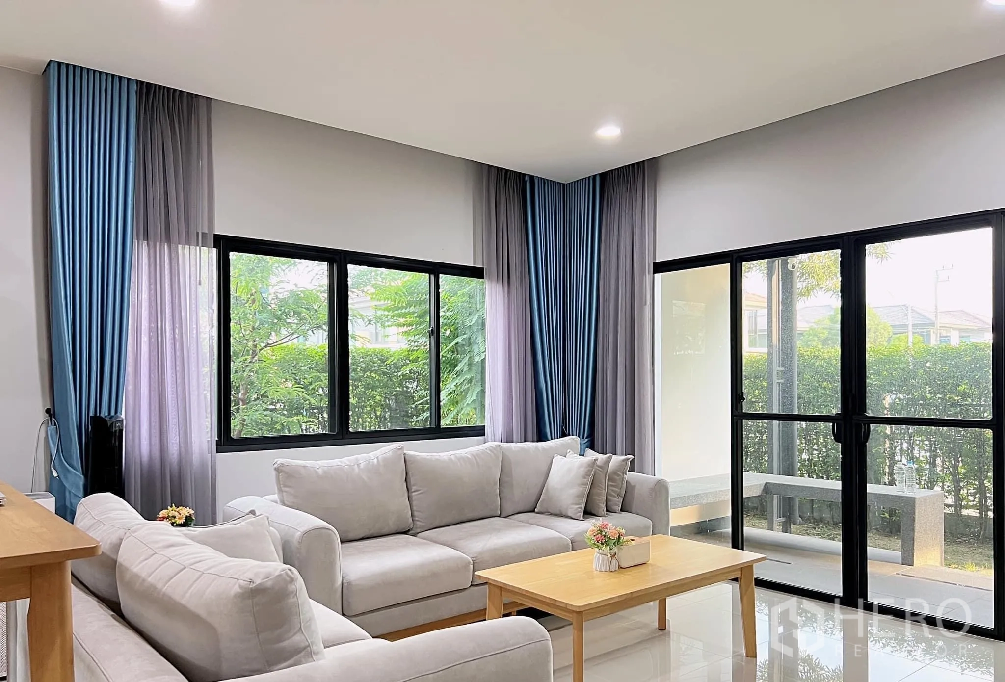 Detached House for rent or sale in Lam Luk Ka, Pathum Thani - Bright living room with large windows, sliding doors, light sofas and garden view.