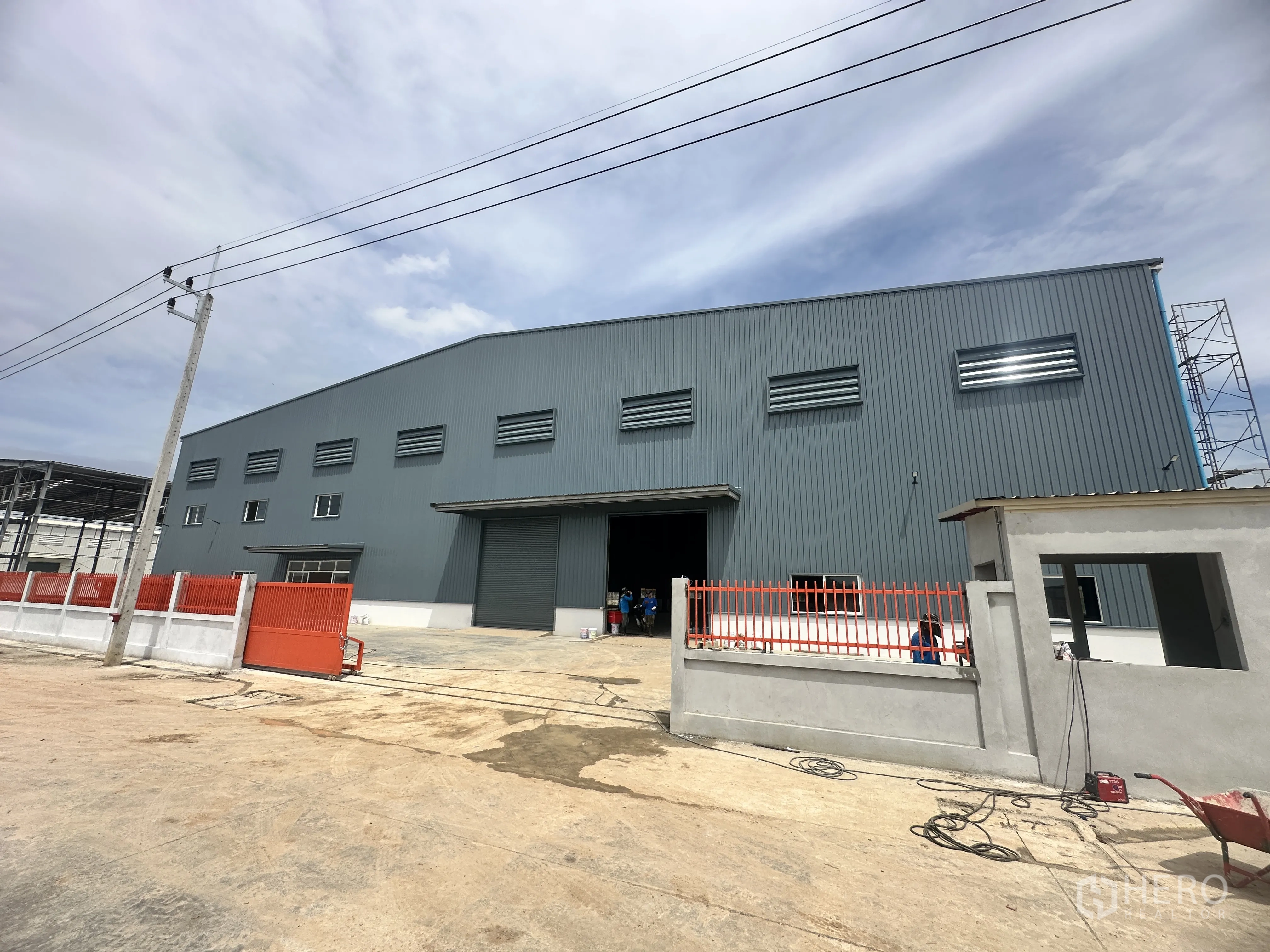Warehouse for rent or sale in Lam Luk Ka, Pathum Thani - Angled exterior view of the warehouse showing the perimeter fence and large entry.