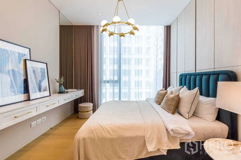 Condominium for sale in Pathum Wan, Bangkok - Second bedroom with teal headboard, chandelier and paneled wall