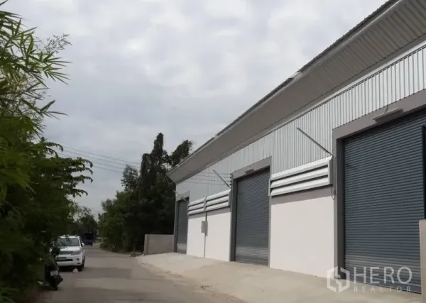 Warehouse for rent in Nonthaburi - Modern warehouse exterior with corrugated metal cladding and multiple roll-up doors along a quiet lane.