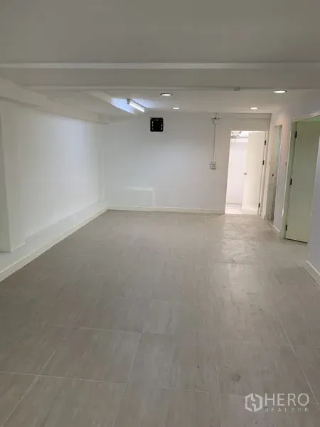 Shophouse for rent in Bang Na, Bangkok - Elongated room with light tiles, white walls, and a doorway to the service area.