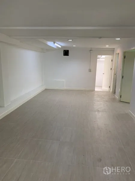 Shophouse for rent in Bang Na, Bangkok - Elongated room with light tiles, white walls, and a doorway to the service area.