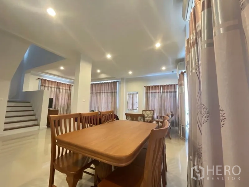 Detached House for sale in Lat Krabang, Bangkok - Open-plan dining area with wooden table set, recessed ceiling lights and stairs nearby.