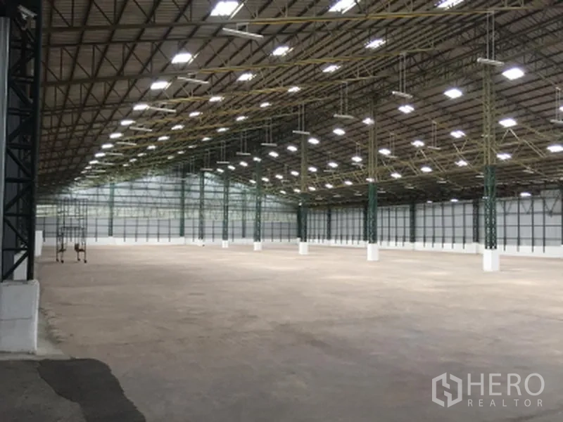 Warehouse for rent in Mueang Pathum Thani, Pathum Thani - Expansive warehouse interior with high steel-truss roof, bright LED lighting and smooth concrete floor.