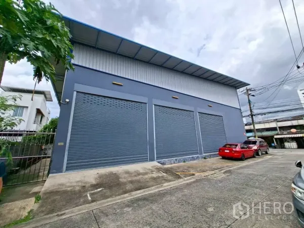 Warehouse for rent in Suan Luang, Bangkok - Street-facing warehouse exterior with three large roller shutters and marked parking bays.