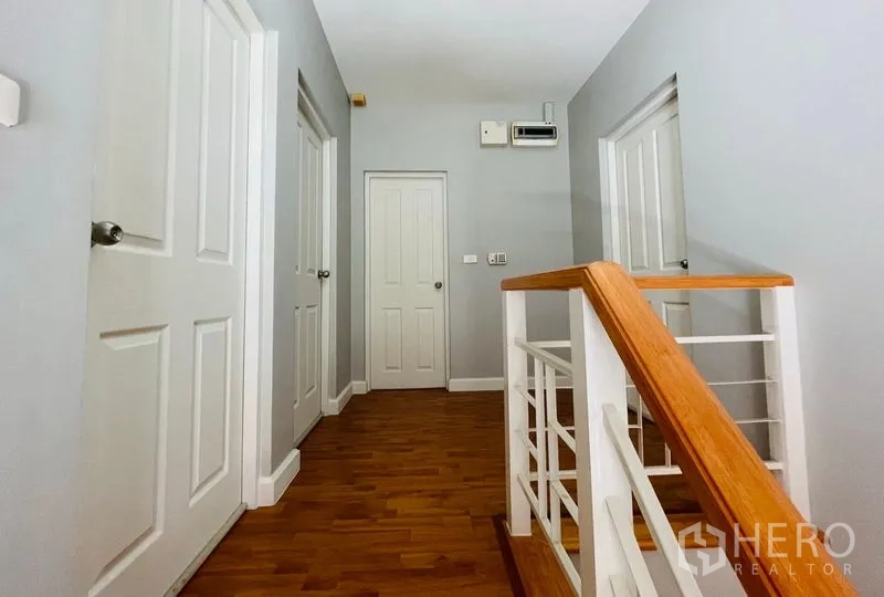 Detached House for sale in Lam Luk Ka, Pathum Thani - Upper hallway with wooden staircase, white doors and warm wood flooring.