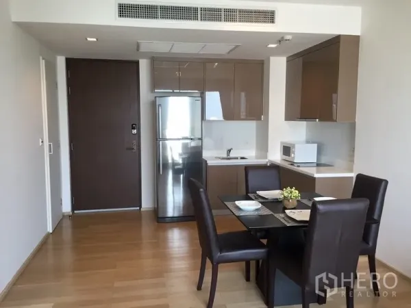 Condominium for rent in Khlong Toei, Bangkok - Open-plan condo entry with glossy kitchenette, stainless fridge and a four-seat dining set on light wood floors.