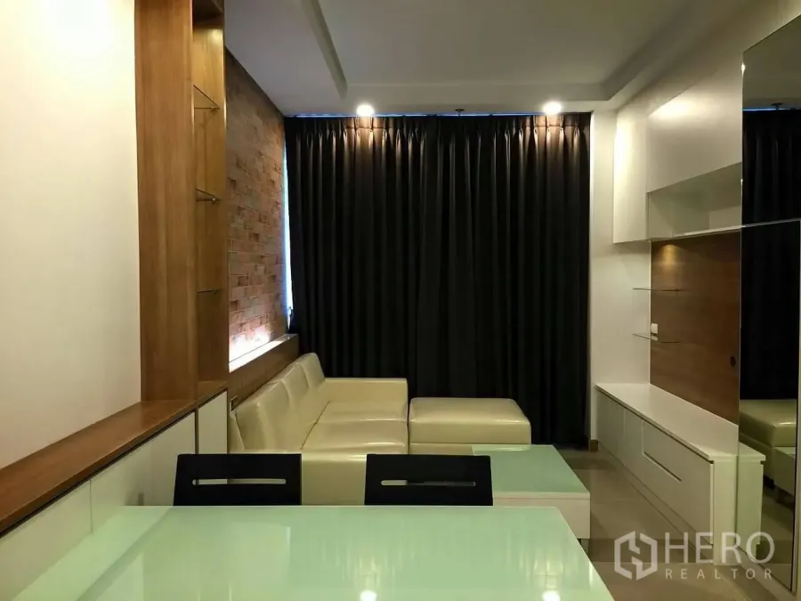 คอนโด ขายในHuai Khwang, Bangkok - ห้องนั่งเล่นสไตล์โมเดิร์น โซฟาเข้ามุมสีครีม ผนังก่ออิฐตกแต่ง ตู้ทีวีบิลต์อิน และผ้าม่านทึบในคอนโดห้วยขวาง