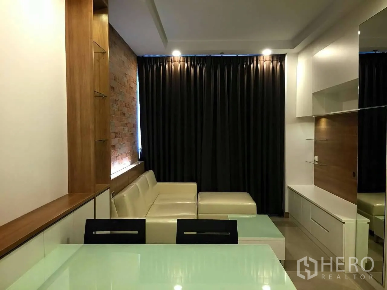 คอนโด ขายในHuai Khwang, Bangkok - ห้องนั่งเล่นสไตล์โมเดิร์น โซฟาเข้ามุมสีครีม ผนังก่ออิฐตกแต่ง ตู้ทีวีบิลต์อิน และผ้าม่านทึบในคอนโดห้วยขวาง