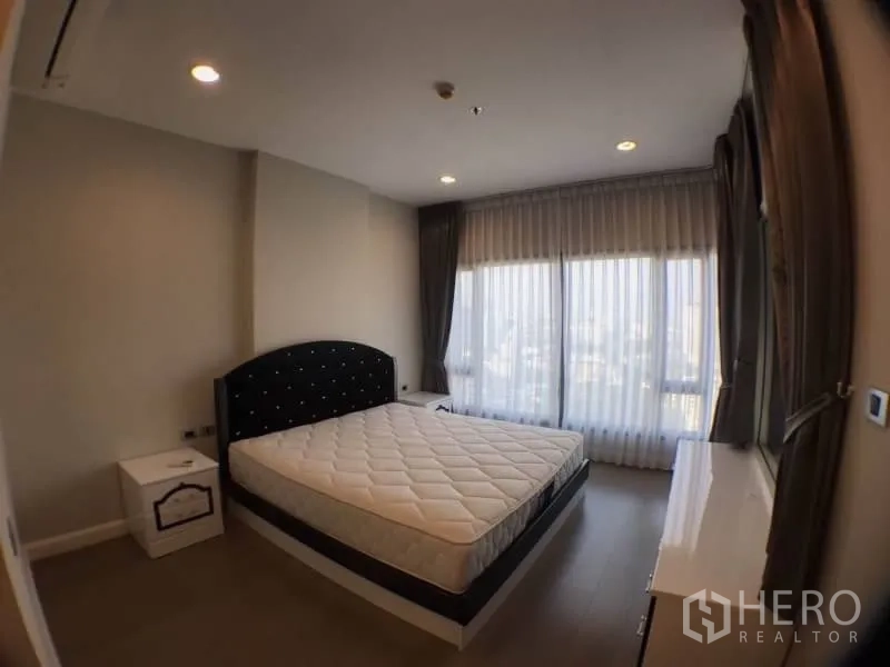 Condominium for rent in Khlong Toei, Bangkok - Master bedroom with large corner windows, bed and soft drapes.