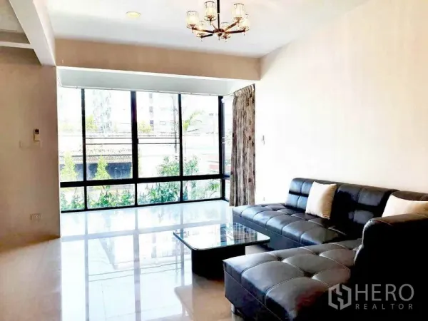 Detached House for rent in Phra Khanong, Bangkok - Sunlit living room with floor-to-ceiling windows and a black leather sectional sofa.