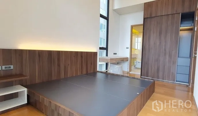 Condominium for sale in Watthana, Bangkok - Primary bedroom with platform bed, wood panel headboard, sliding wardrobe, and ensuite access.