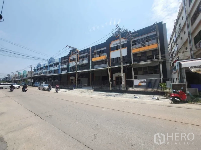 Factory for rent or sale in Samut Prakan - Three-storey industrial row building with gated fronts and scaffolding along a wide street in Bang Phli.