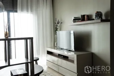 Condominium for rent in Phaya Thai, Bangkok - Another view of the living area showing media cabinet, floating shelf and soft daylight through drapes.