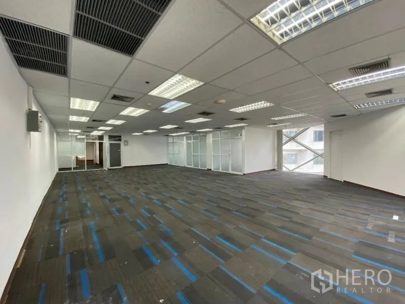 Office Space for rent in Khlong Toei, Bangkok - Spacious open-plan office with blue-striped carpet tiles, drop ceiling, fluorescent lighting and glass-partitioned rooms.