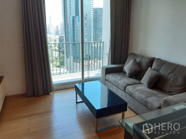 Condominium for rent in Khlong Toei, Bangkok - Bright living room with gray sofa, glass coffee table and balcony overlooking the Bangkok skyline