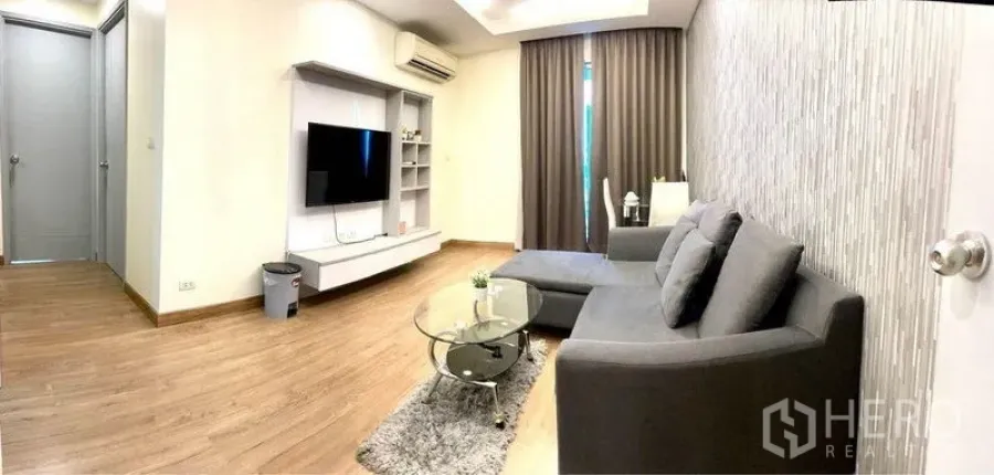 Condominium for rent in Huai Khwang, Bangkok - Open-plan living area with TV console, sectional sofa and floor-to-ceiling curtains.