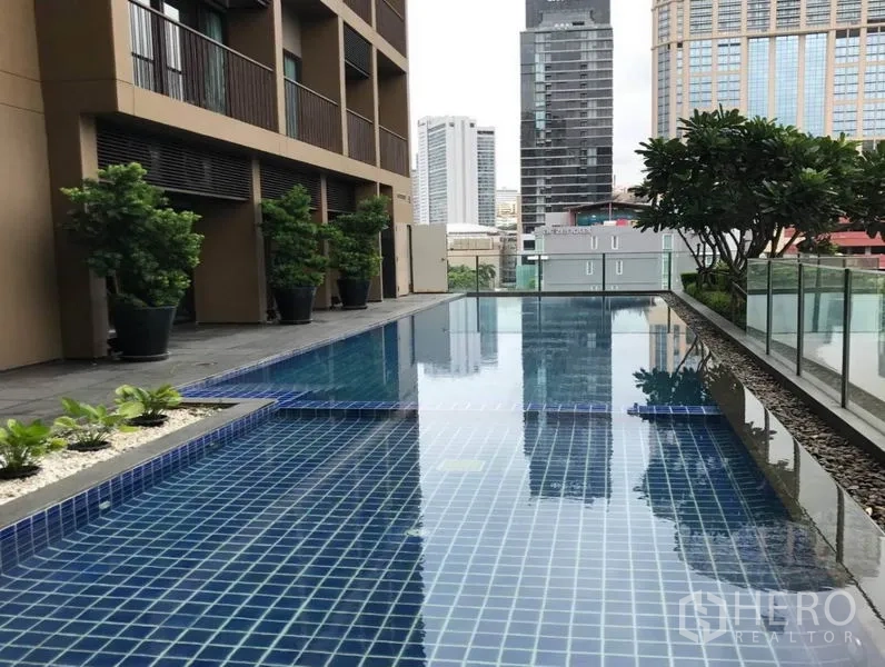 Condominium for rent in Bangkok - Outdoor lap pool with blue tiles, greenery, and city buildings in the background.