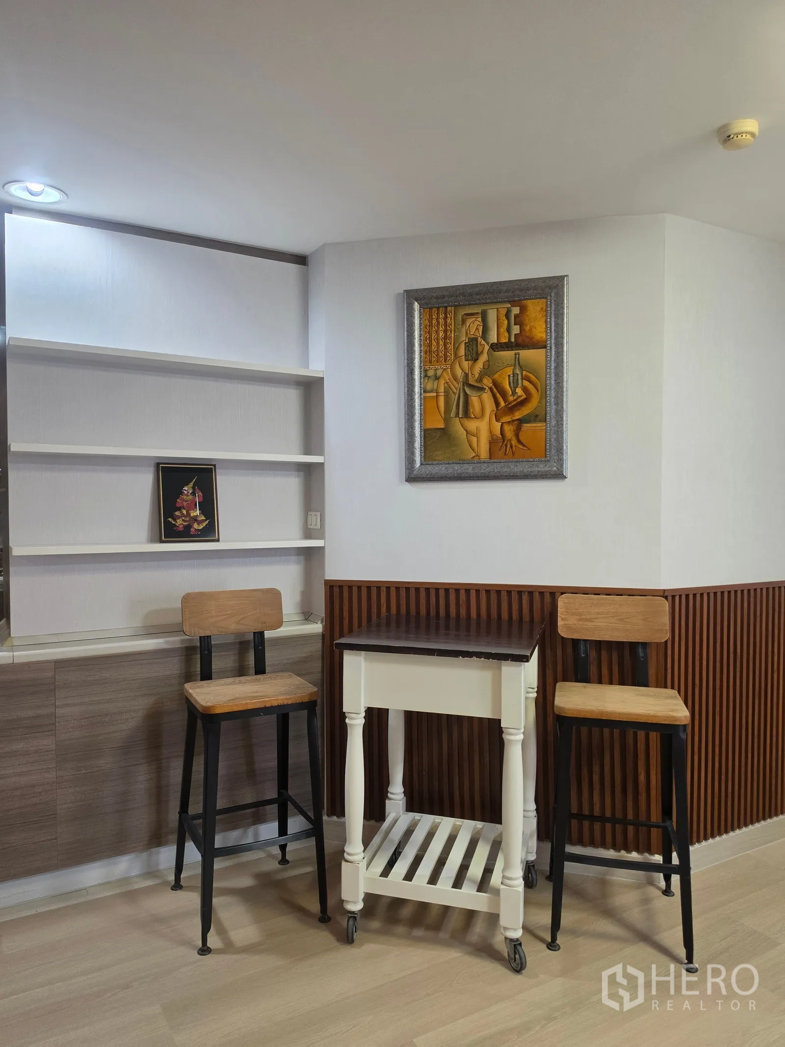 Condominium for rent in Huai Khwang, Bangkok - Corner nook with two bar stools, rolling cart, shelves, and framed art.
