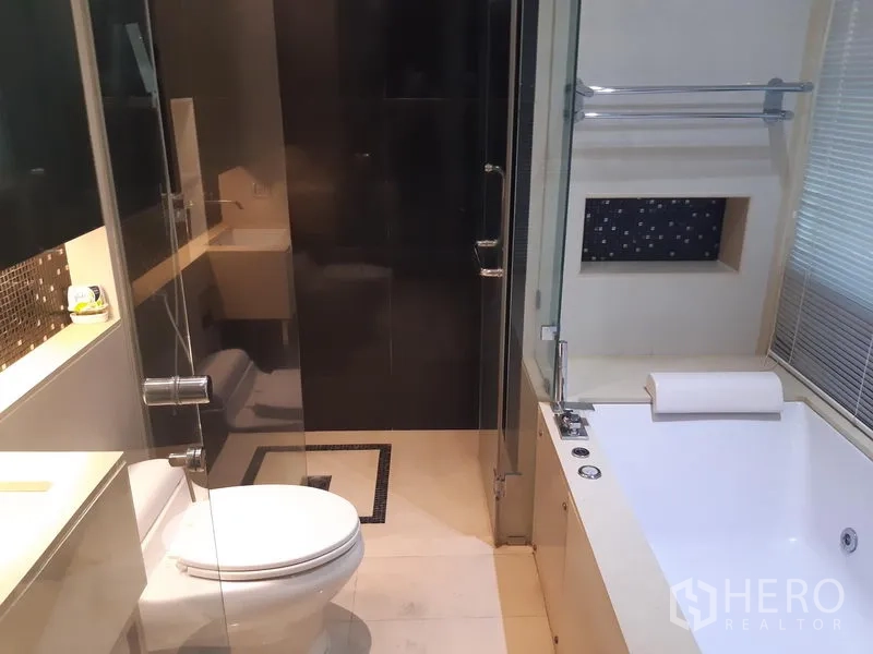 Condominium for rent or sale in Khlong Toei, Bangkok - Modern bathroom with glass shower, bathtub, toilet and vanity.