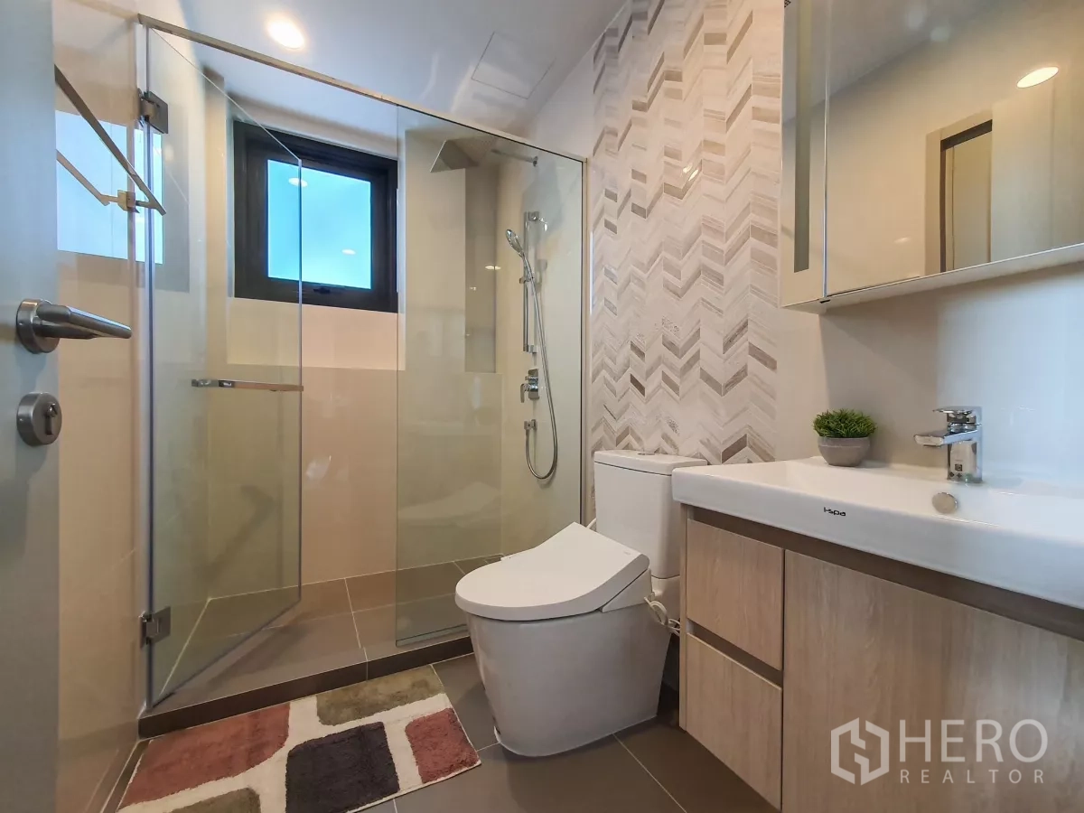Condominium for rent in Khlong Toei, Bangkok - Modern bathroom with glass shower, vanity and patterned tile wall.