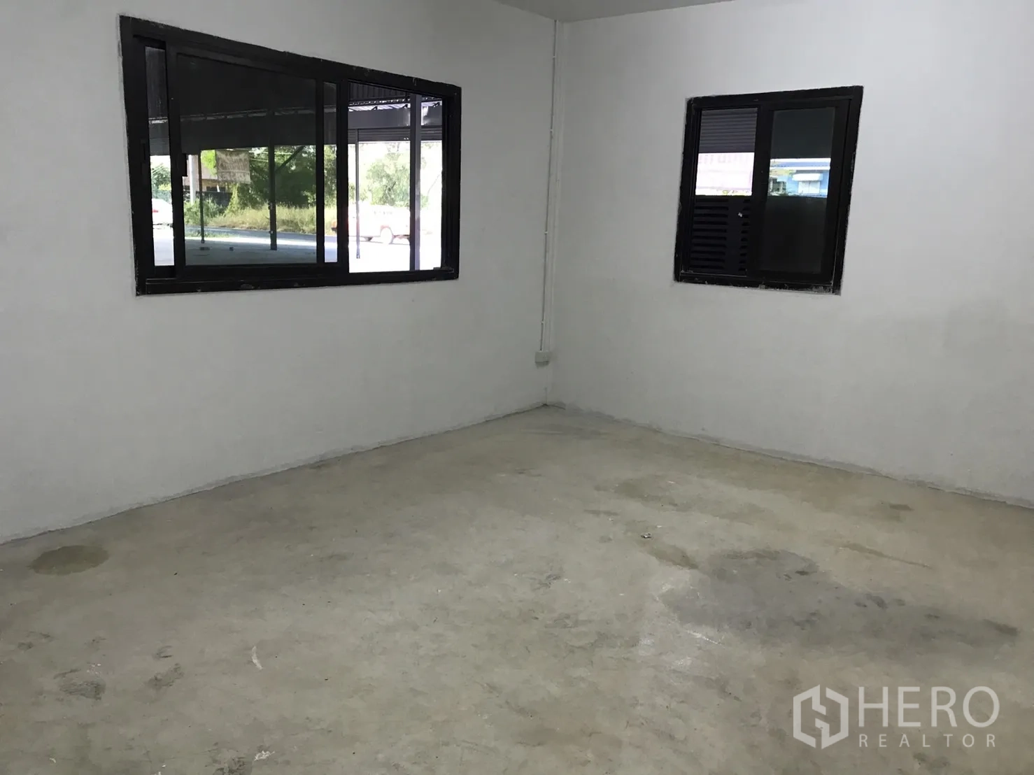 Warehouse for rent in Lam Luk Ka, Pathum Thani - Empty office room with two windows and unfinished concrete floor.