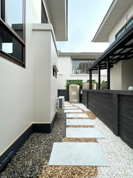 独立式住宅 出售在Bang Kapi, Bangkok - 侧院铺卵石与踏步石小径，沿篱笆设水箱与空调外机。