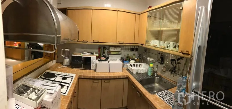 Condominium for rent in Bang Rak, Bangkok - Compact L-shaped kitchen with gas hob, sink, tiled countertop and light wood cabinetry.
