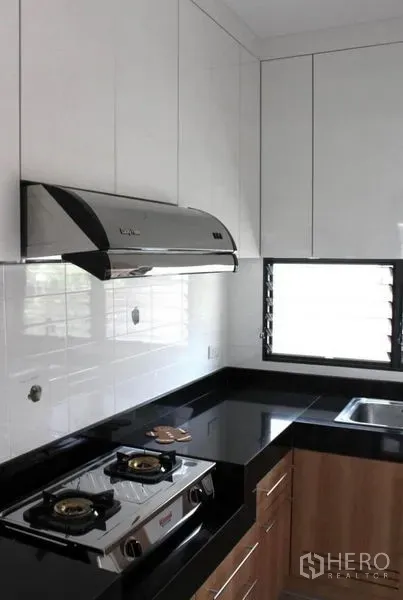 Detached House for rent in Prawet, Bangkok - Modern Thai kitchen with gas hob, range hood, black granite countertops and white cabinets.