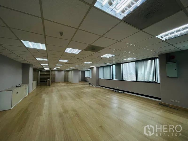 Office Space for rent - Spacious open‑plan office with wood flooring, grid ceiling lights, and large windows with vertical blinds.