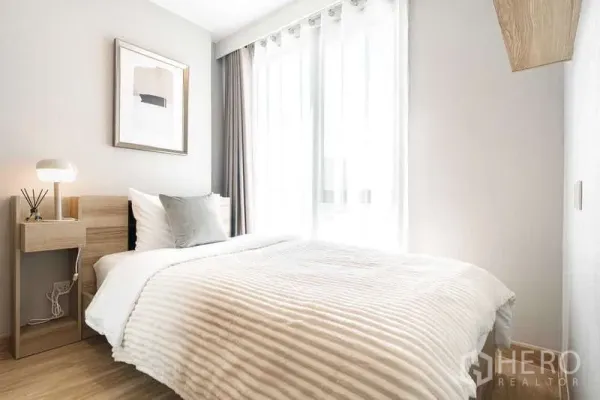 Condominium for rent - Sunny bedroom with double bed, bedside table, and floor-to-ceiling curtains.