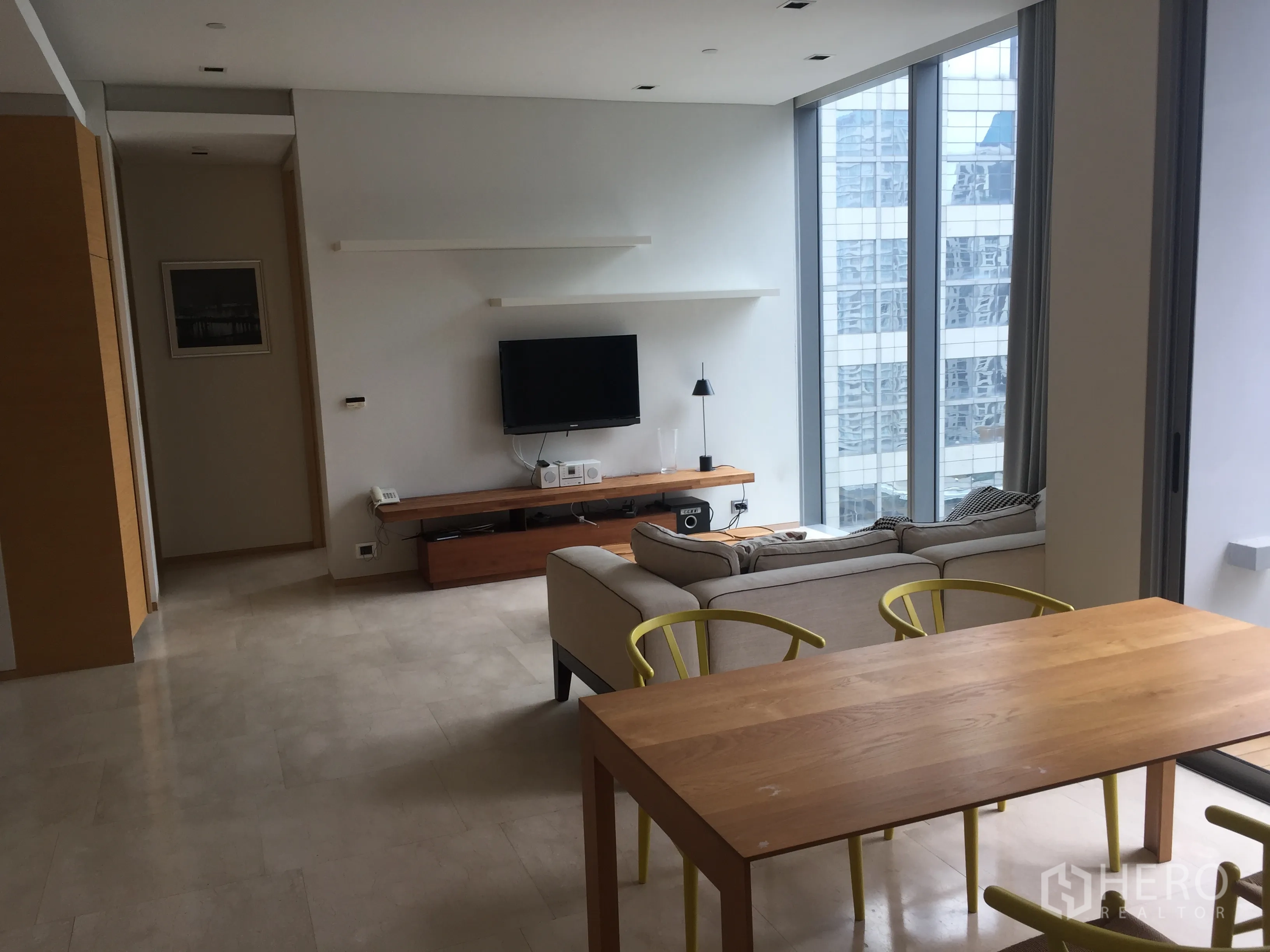 Condominium for rent in Bang Rak, Bangkok - Open-plan living and dining area with floor-to-ceiling windows, city views, a wood table and a cozy sofa in a modern Bangkok condo.