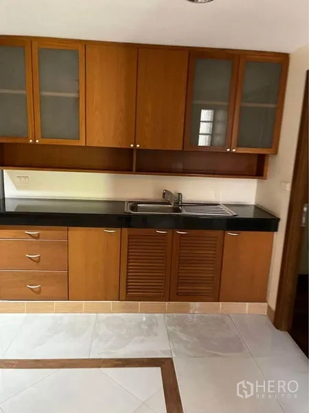 Townhouse for sale in Phra Khanong, Bangkok - Practical kitchen with wooden cabinets, black countertop, sink, and tiled floor.